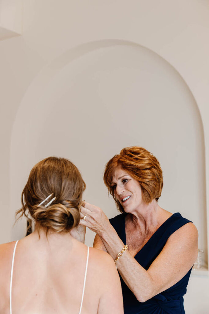 A person helping put jewelry on a wedding participant 