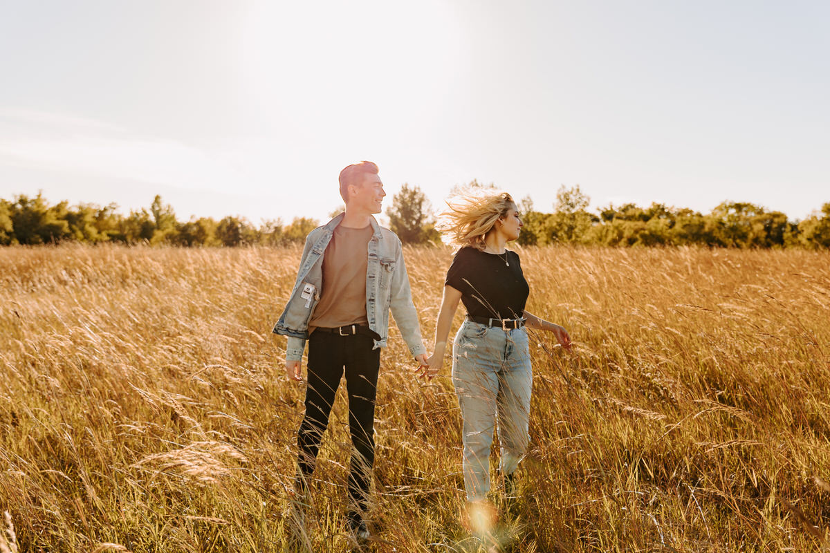 Adventure engagement photos of a couple holding hands and running through a field