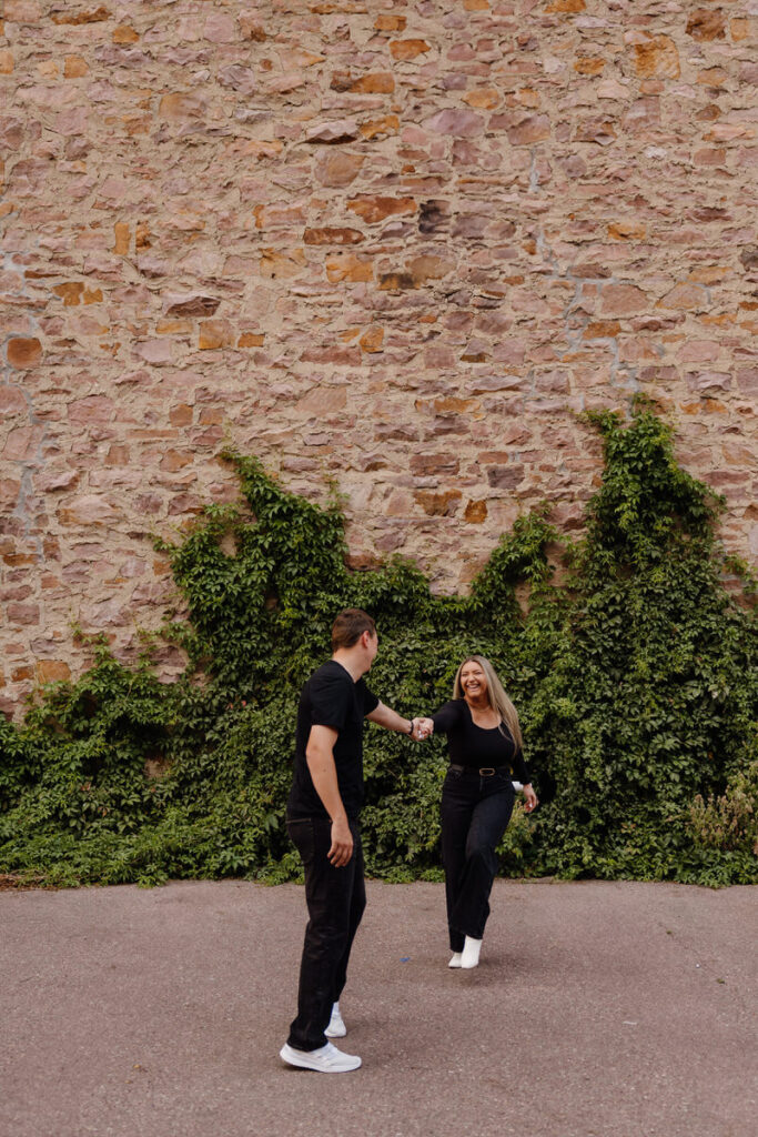 A couple dancing in a small area next to a stone wall 