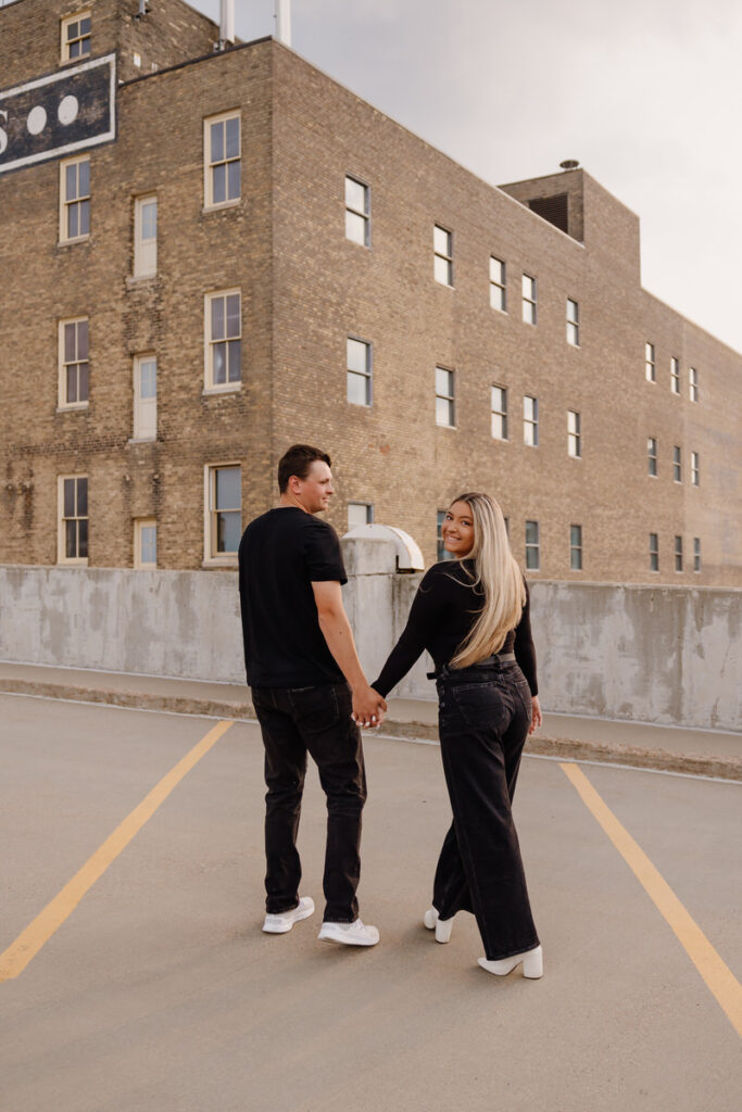 A couple holding hands and walking together on a parking garage rooftop 