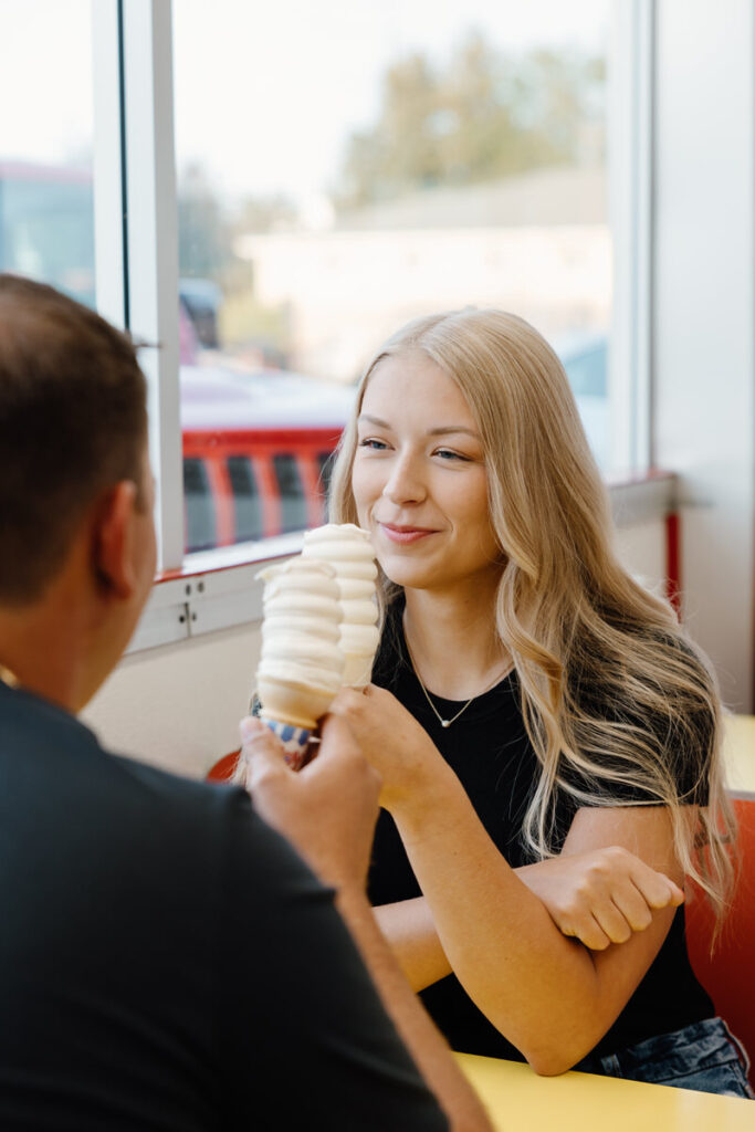 A couple sitting at a booth in an ice cream shop holding ice cream cones 