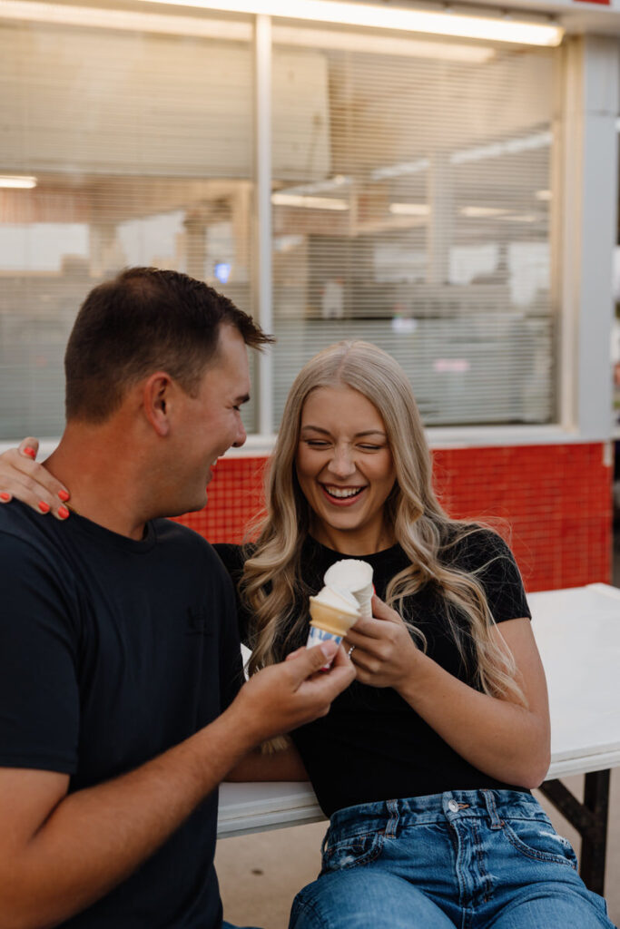 A couple sitting at a picnic table eating ice cream together and smiling 