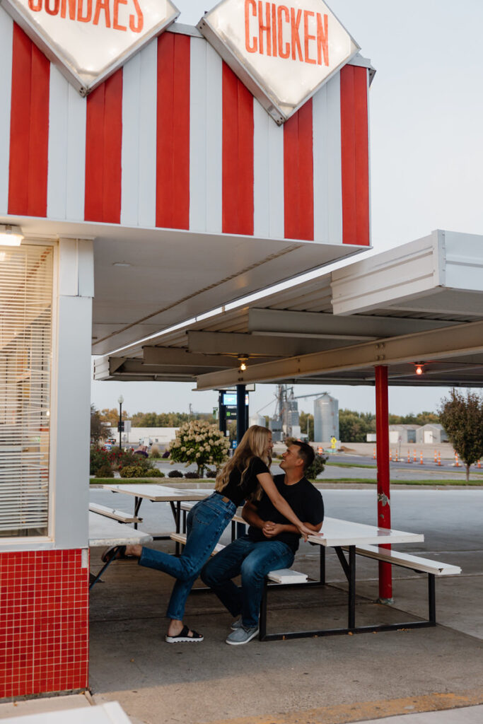 A person leaning over their partner who is sitting at a picnic table. 