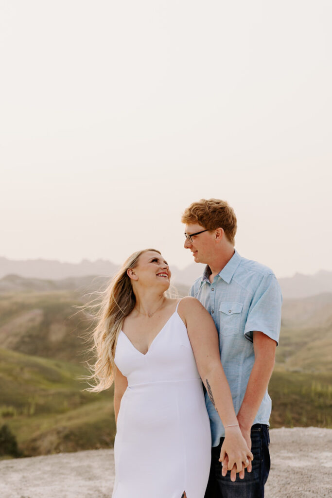 A couple standing one behind the other holding hands and smiling at each other 