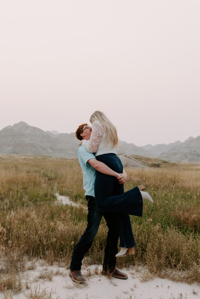 A person holding up their partner as they smile in a field. 