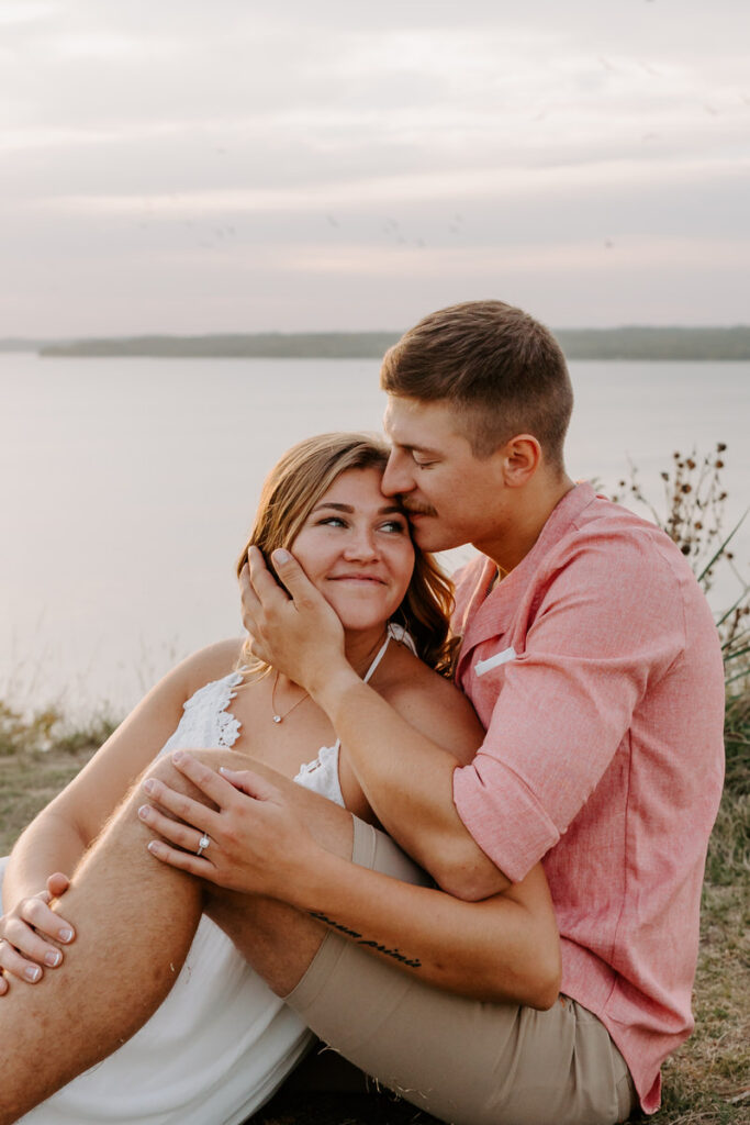 A couple sitting together in the grass with their arms around each other 