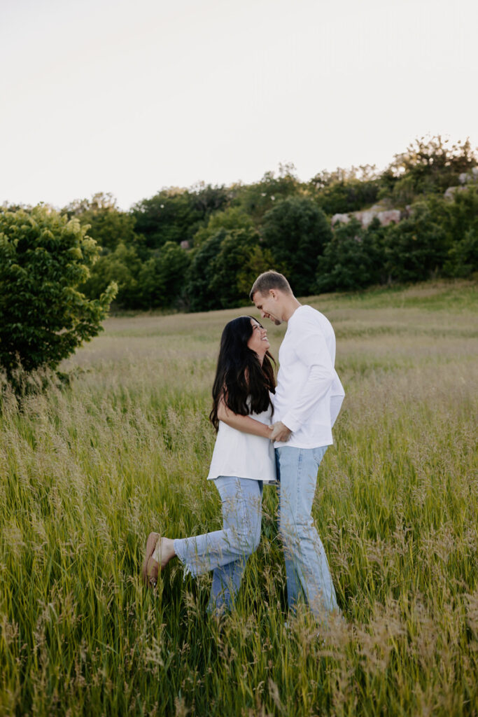 A couple dancing together in tall grass smiling 