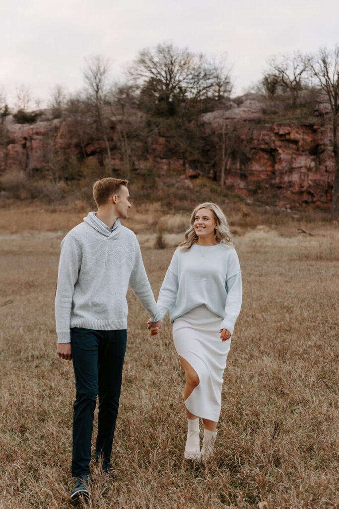 A couple holding hands and walking in a field 