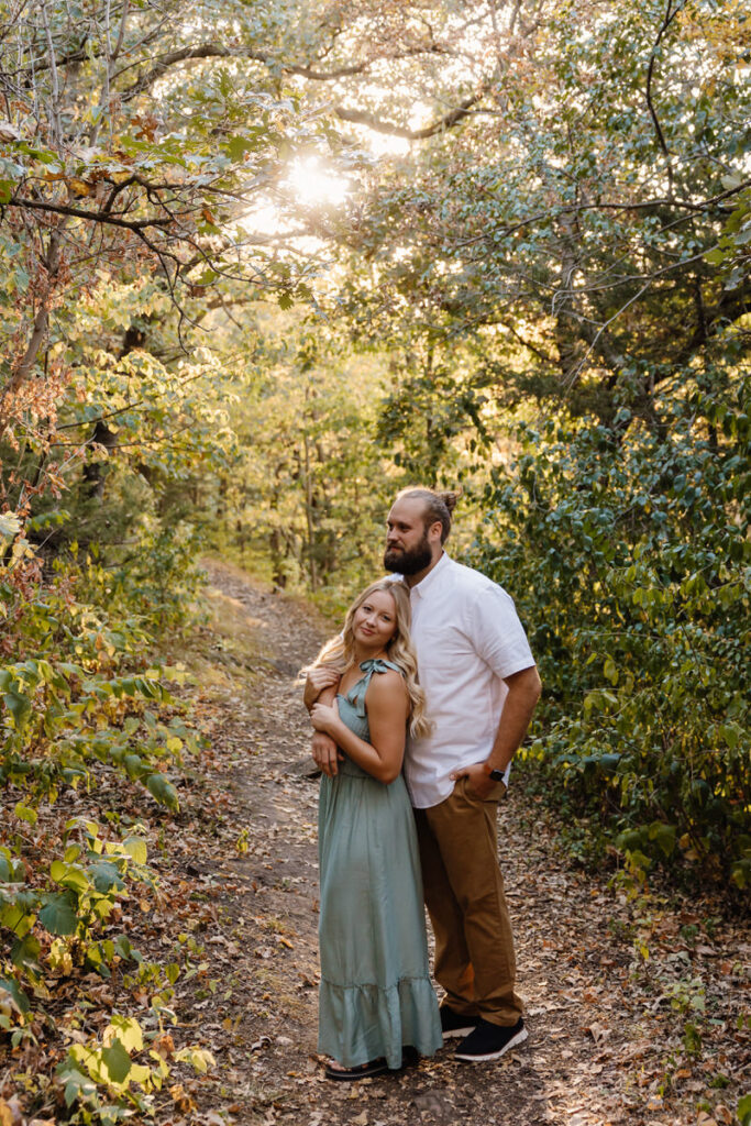 A couple standing together on a walking trail in the woods 
