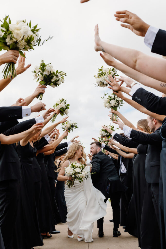 A wedding couple dancing in between their wedding parties with their arms up 