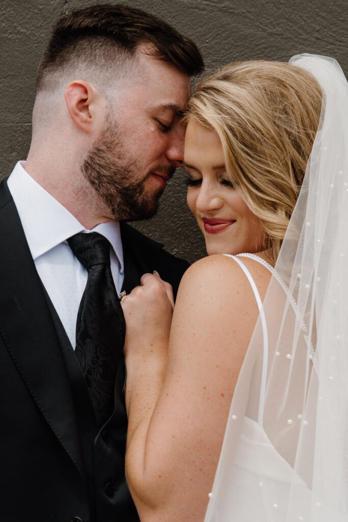 A newlywed couple standing close together with their foreheads touching 