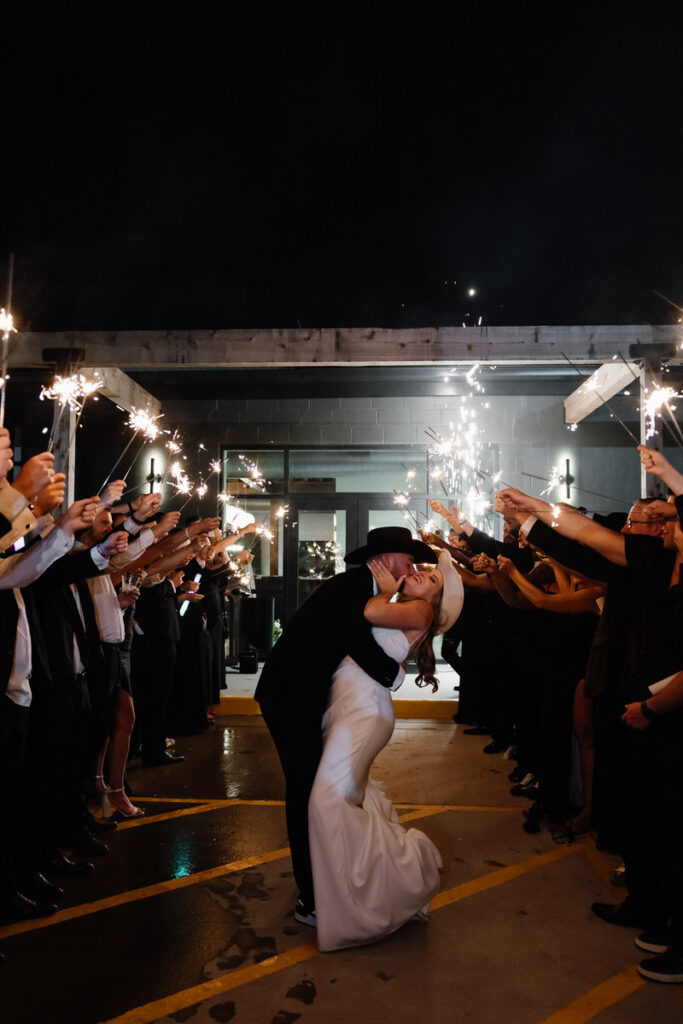 Newlyweds kissing with their guests holding up sparklers around them 